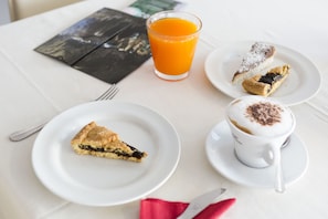 A table with a glass of orange juice, a slice of pie, a pastry, and a cup of coffee.
