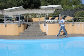 A swimming pool with steps leading into it, surrounded by lounge chairs and umbrellas.