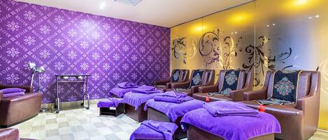 A spa room with multiple massage chairs, a small table with a vase, and patterned walls.