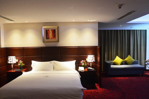 A hotel room with a large bed, a sofa, a painting on the wall, and a red carpet. - Dhaka Regency Hotel & Resort (Dhaka)