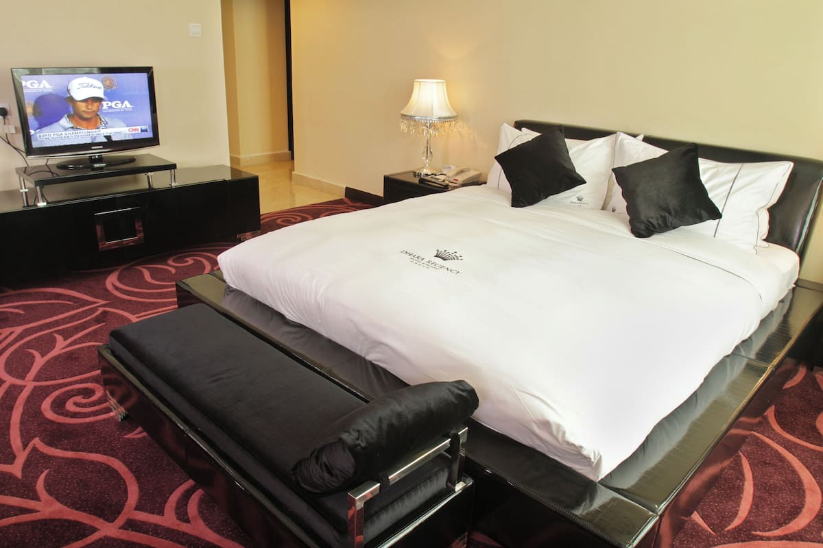 Una habitación de hotel con cama, televisor, mesita de noche y lámpara.