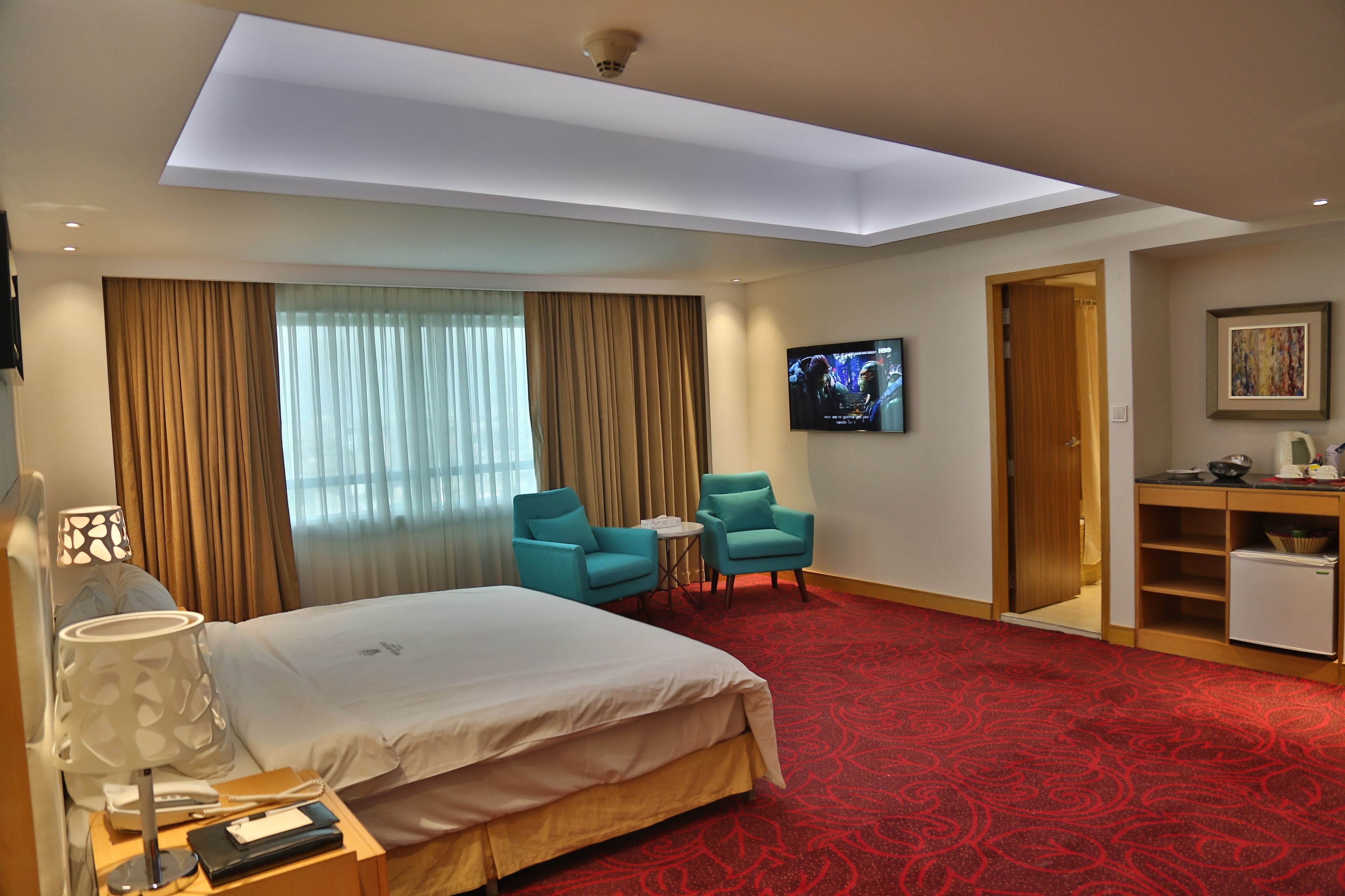 Una habitación de hotel con una cama grande, dos sillas, una mesita, televisor y una kitchenette.