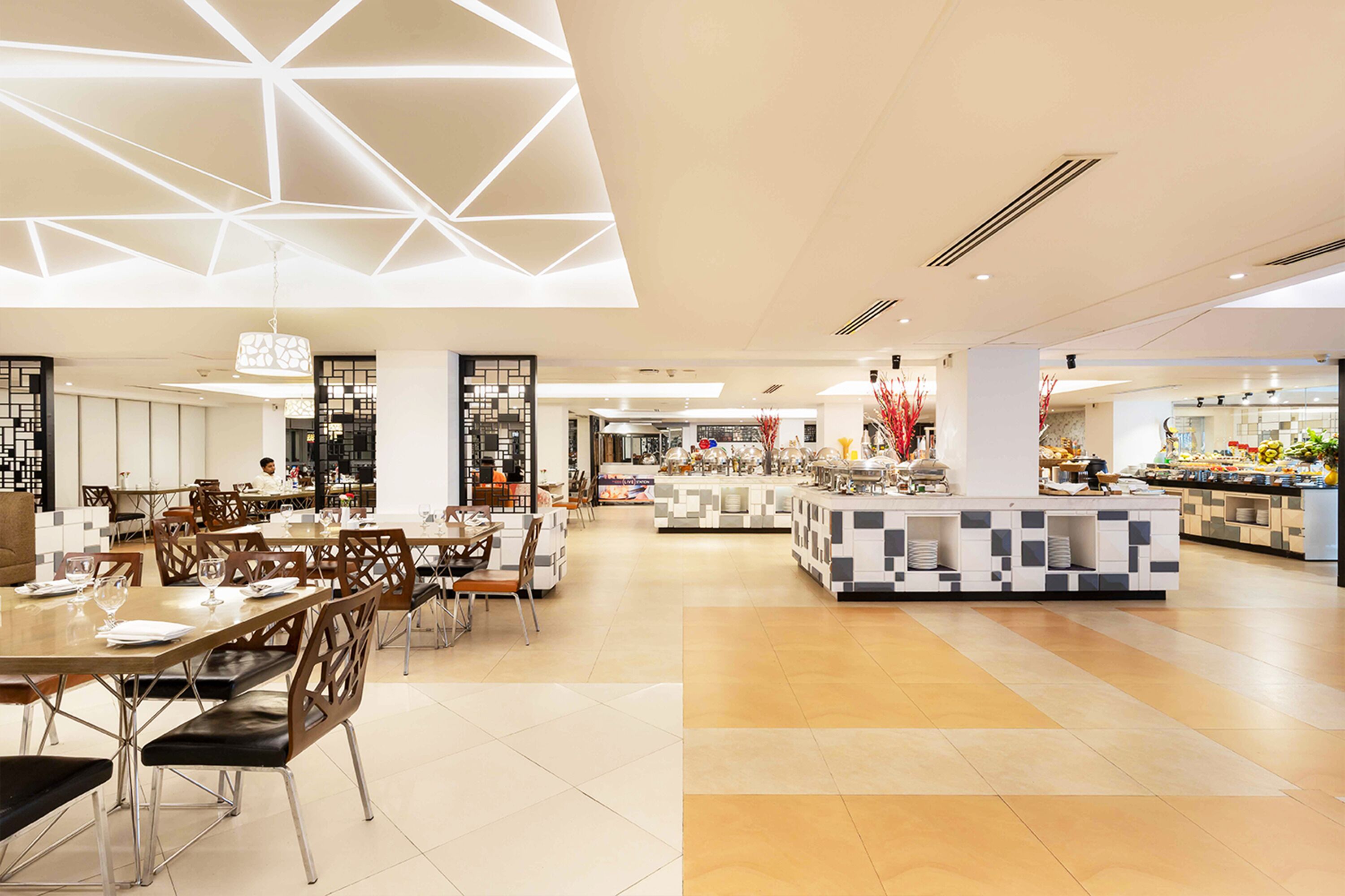 A modern dining area with geometric ceiling design, a central buffet, and a variety of seating arrangements.