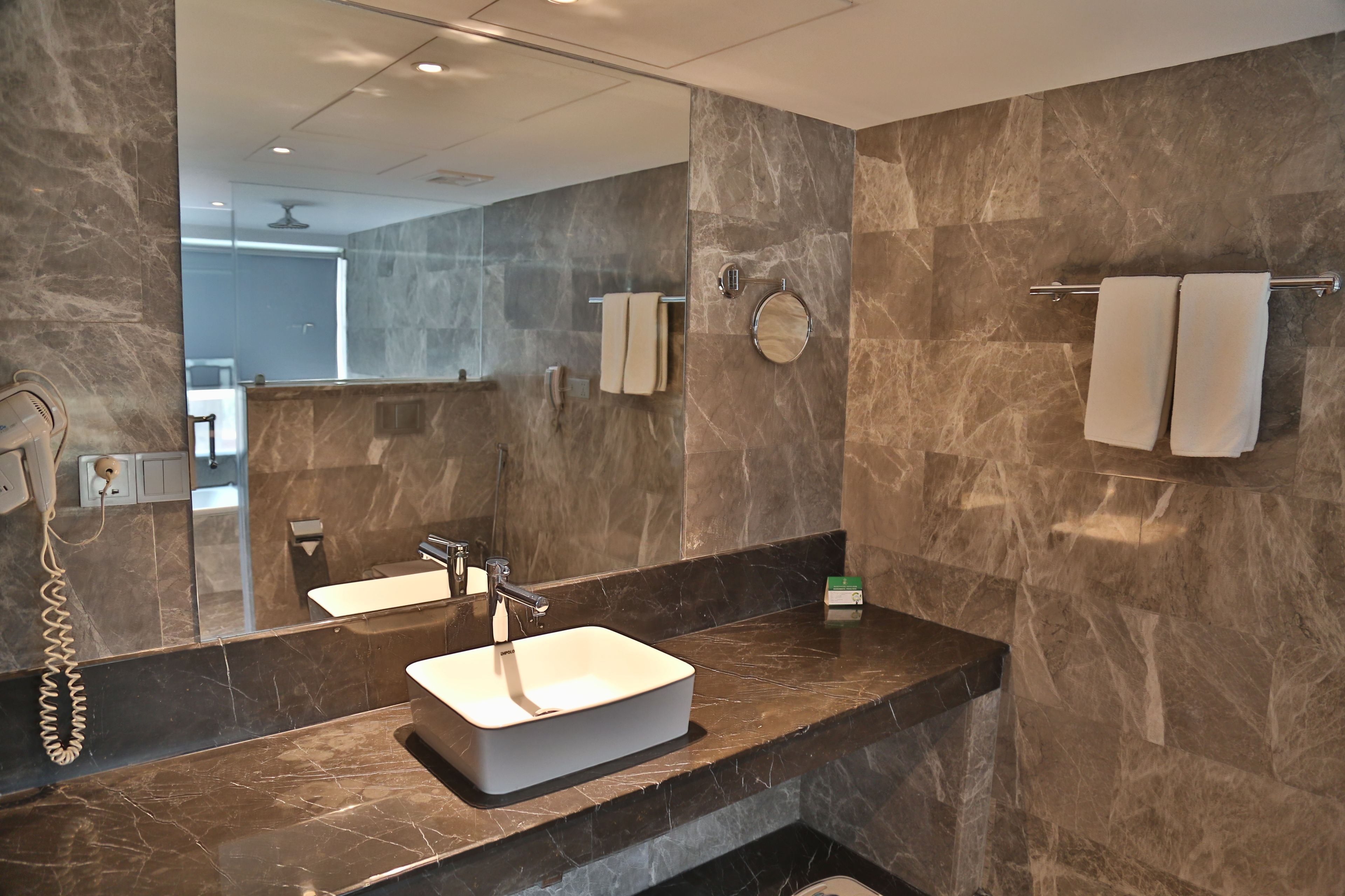 Un baño moderno con un espejo grande, un lavamanos blanco y paredes de mármol.