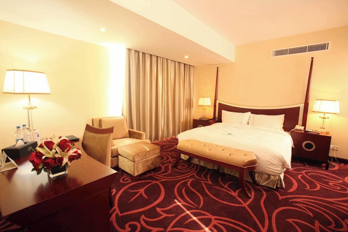 Habitación de hotel con una cama grande, un escritorio, una silla y una mesita con un florero.