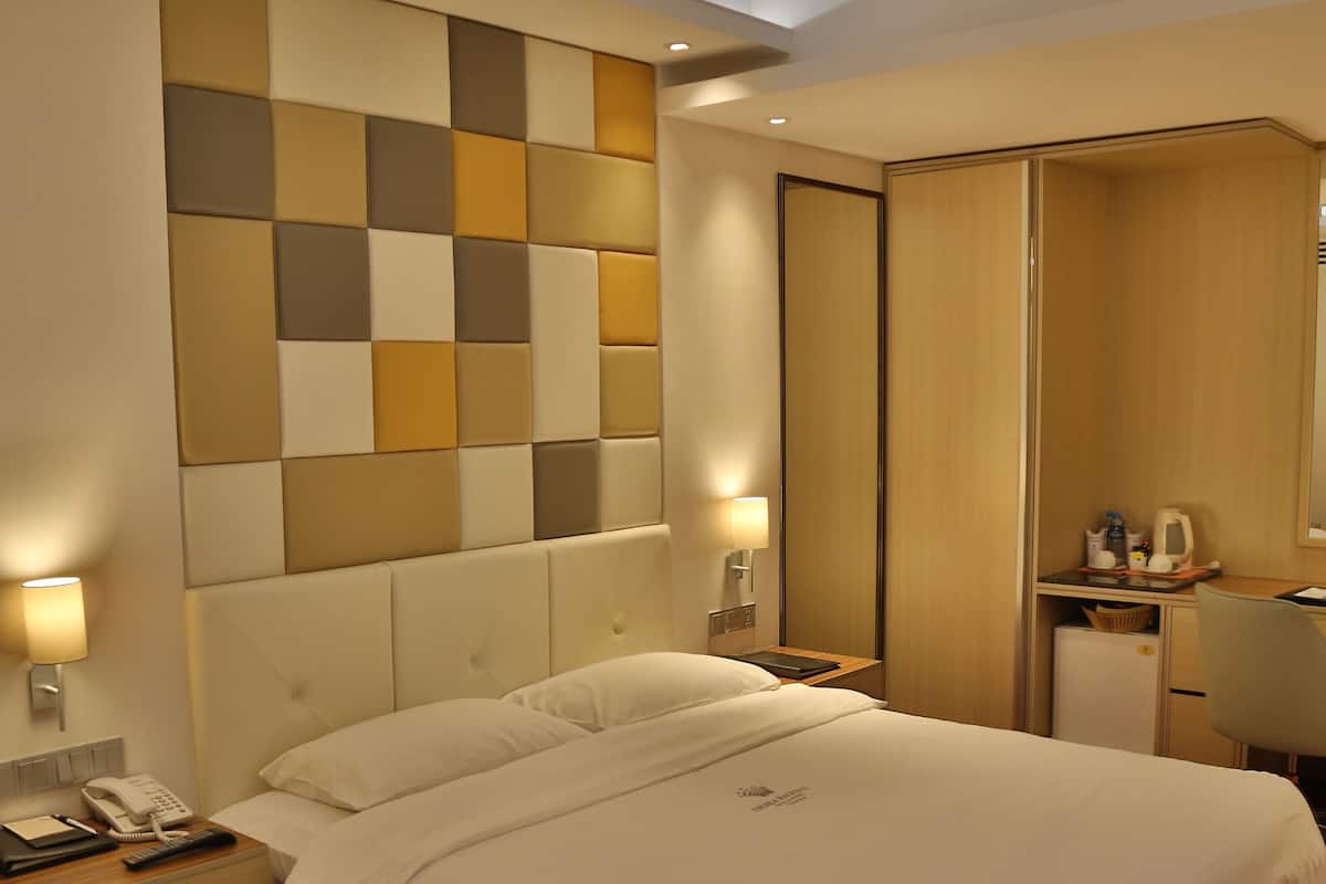Habitación de hotel con cama, mesitas de noche, escritorio con silla, espejo y pared con diseño geométrico.