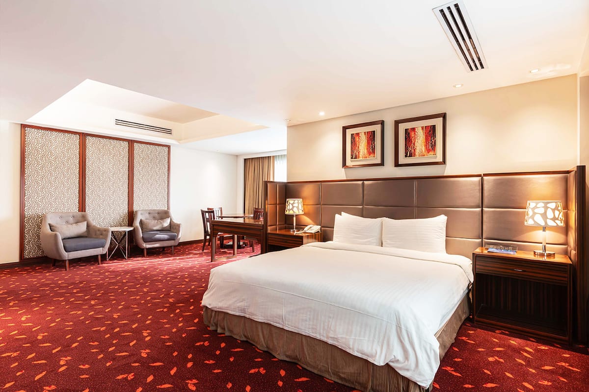 Habitación de hotel con una cama grande, dos mesitas de noche con lámparas, un escritorio con una silla y un separador decorativo.