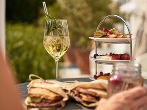 A table with a glass of white wine, a tray of fruit, and sandwiches.