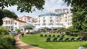 A large, multi-story hotel with a central courtyard, outdoor seating area, and a well-maintained garden.