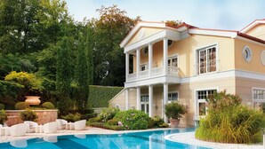 A large, two-story building with a swimming pool, surrounded by lush greenery and outdoor seating.