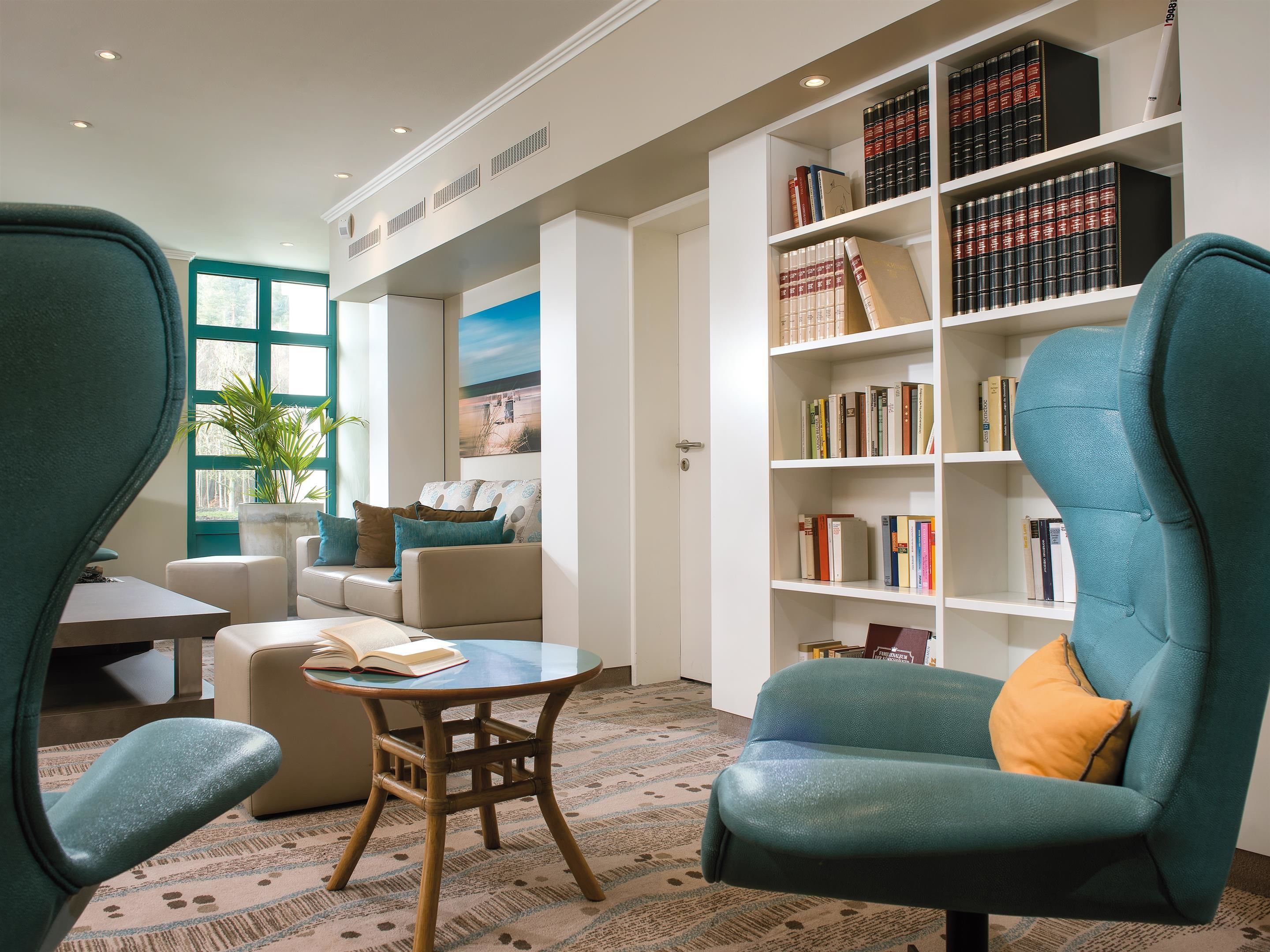 A modern library with teal chairs, a wooden table, and a bookshelf filled with books.