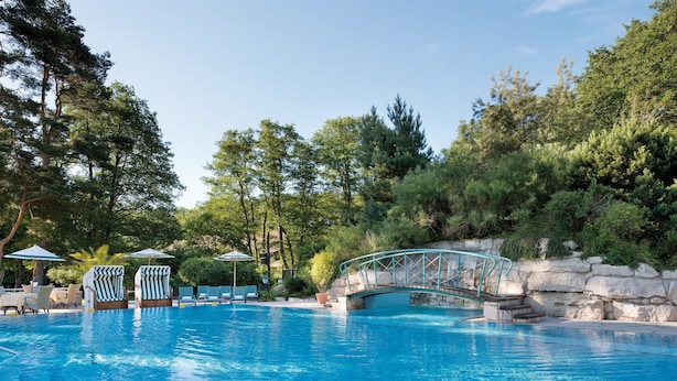 A swimming pool with lounge chairs and umbrellas, surrounded by trees and a stone bridge. - Bernstein Prerow (Ostseebad Prerow)