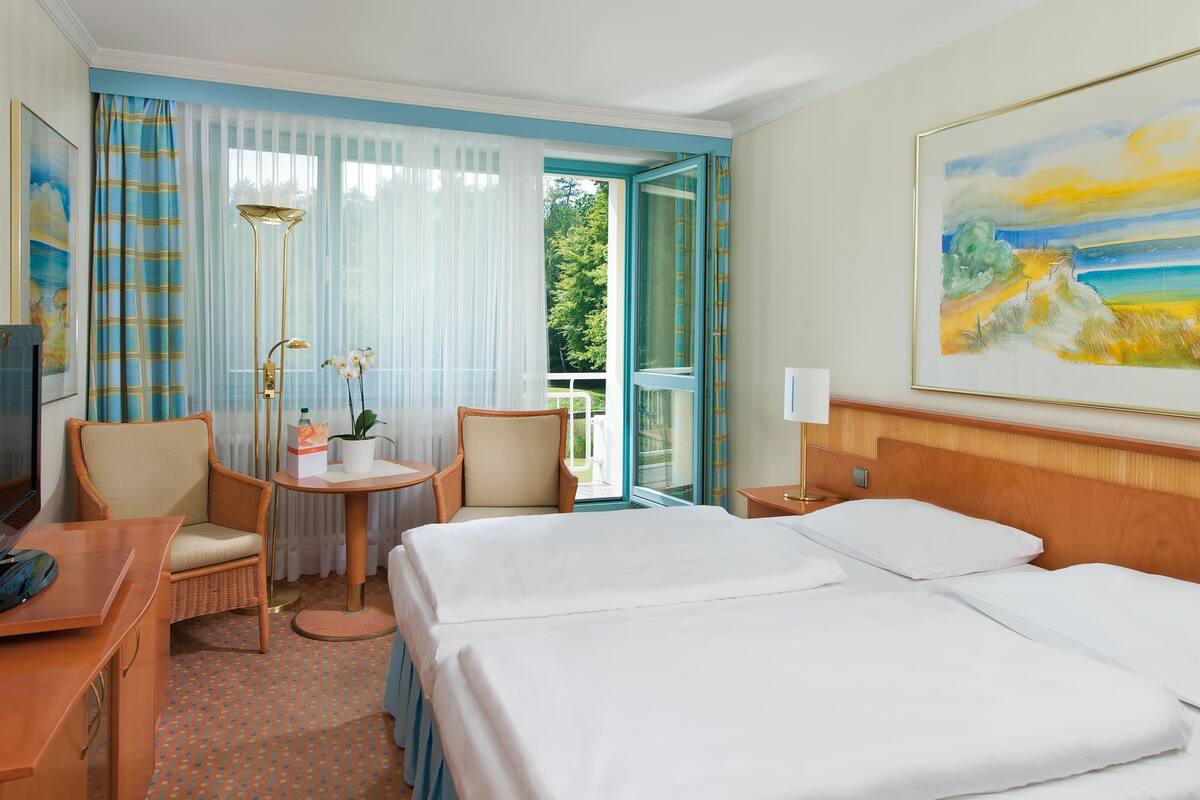 Ein Hotelzimmer mit Bett, Schreibtisch, Stuhl, kleinem Tisch mit Pflanze und einem Bild an der Wand.