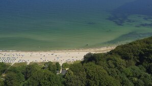 An aerial view of a beach with clear waters, a sandy shore, and dense greenery in the foreground.