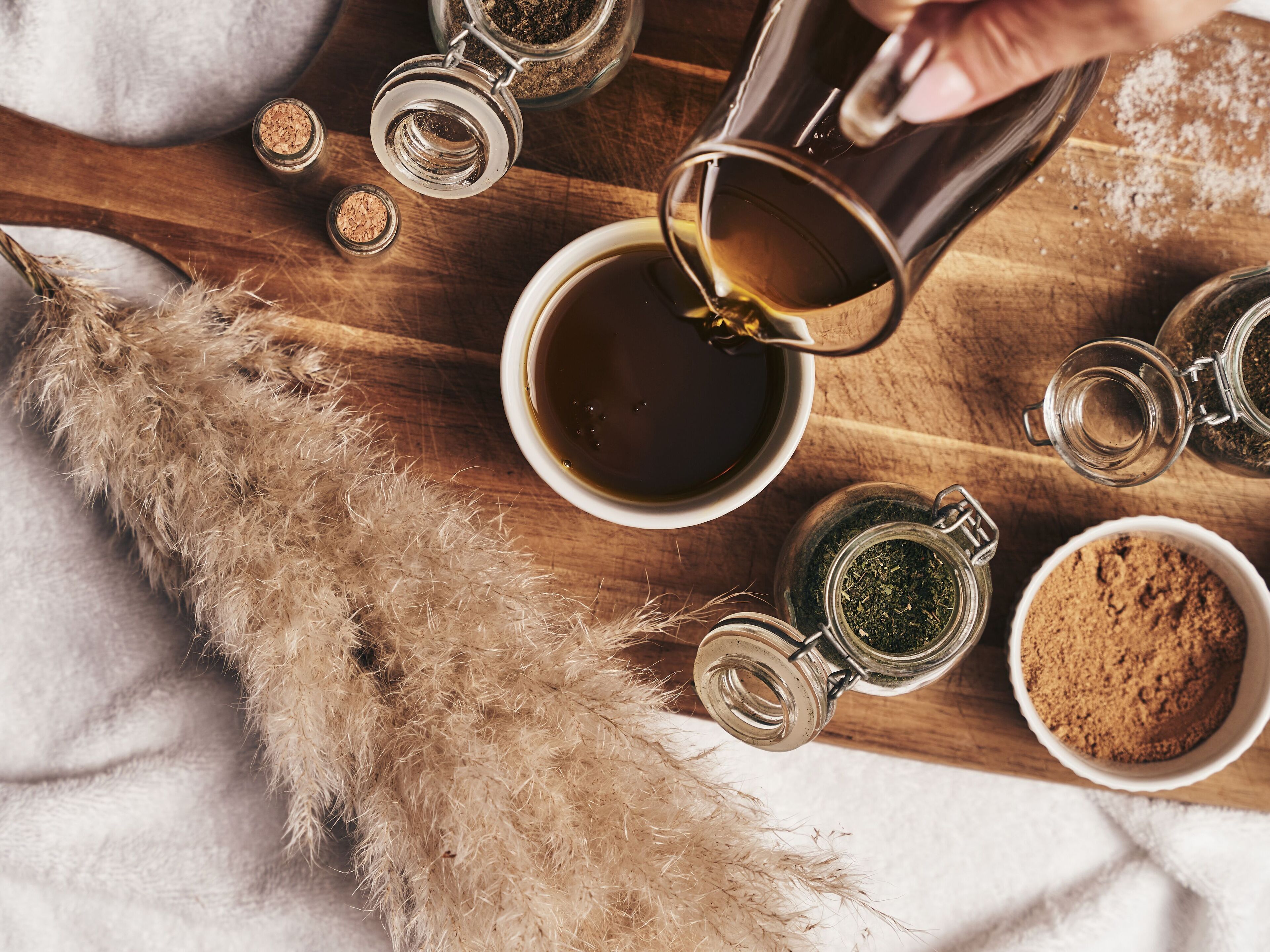 Un plateau en bois avec une tasse de thé, un bocal de thé vert, un bocal de poudre brune et un bol de poudre brune.