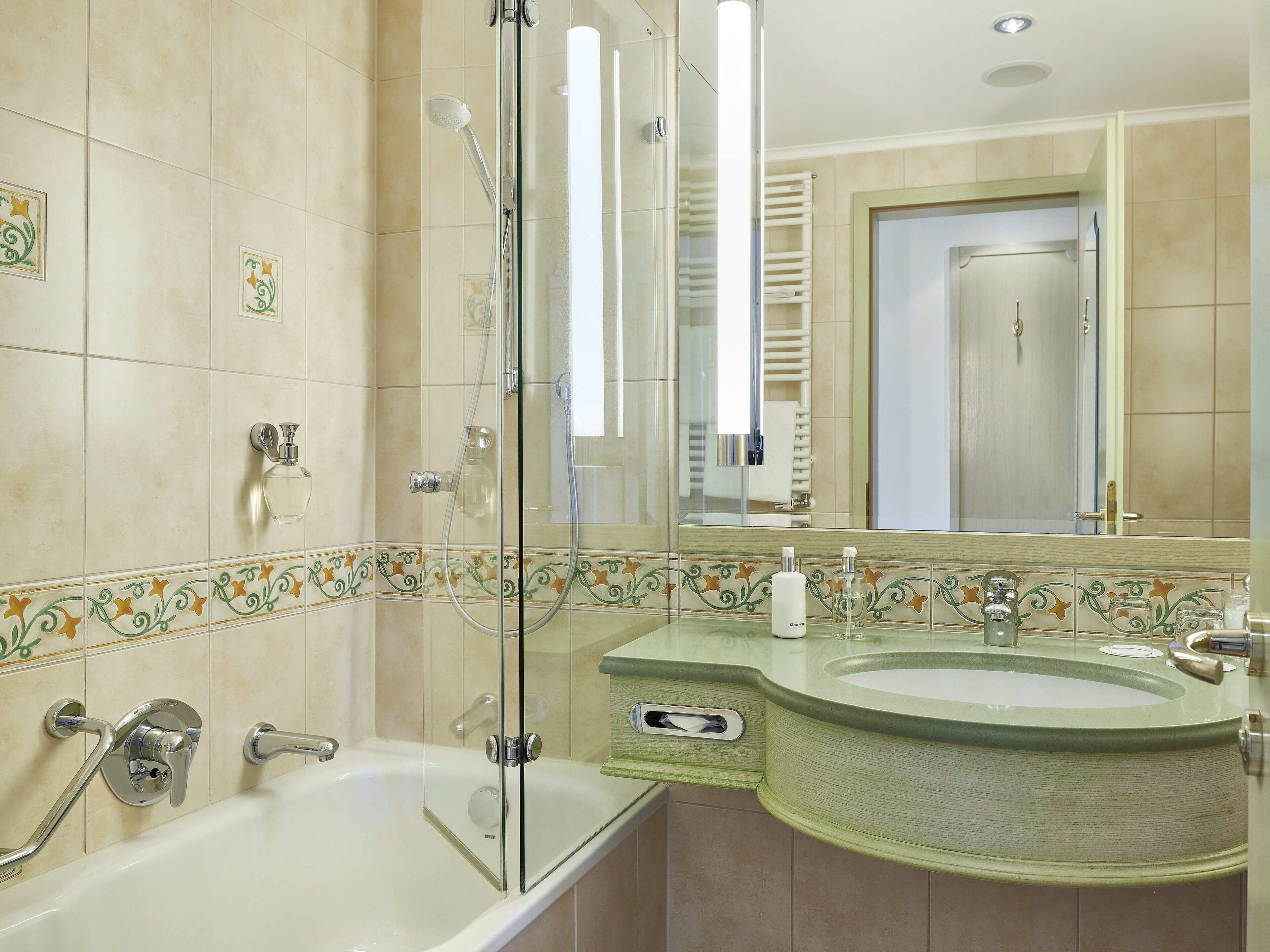 A bathroom with a glass-enclosed shower, a bathtub, and a sink with a green countertop.