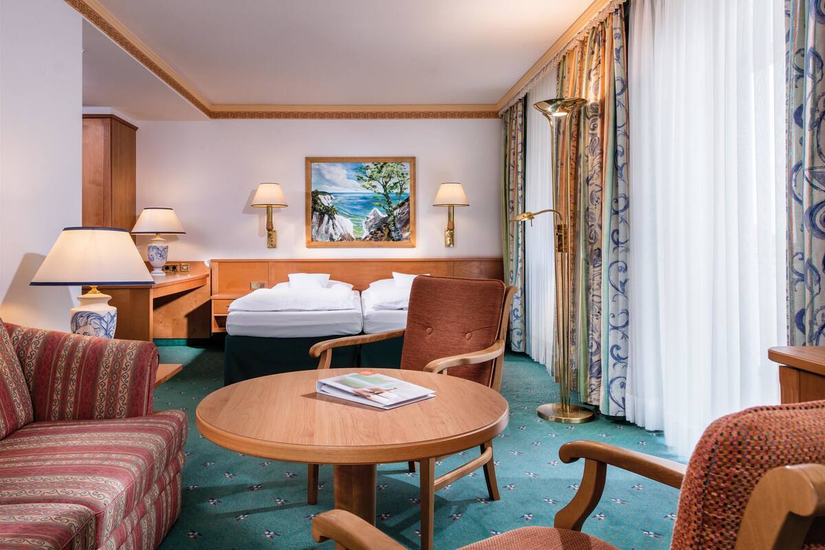 A hotel room with a bed, two bedside lamps, a painting, a round wooden table, and a patterned carpet.