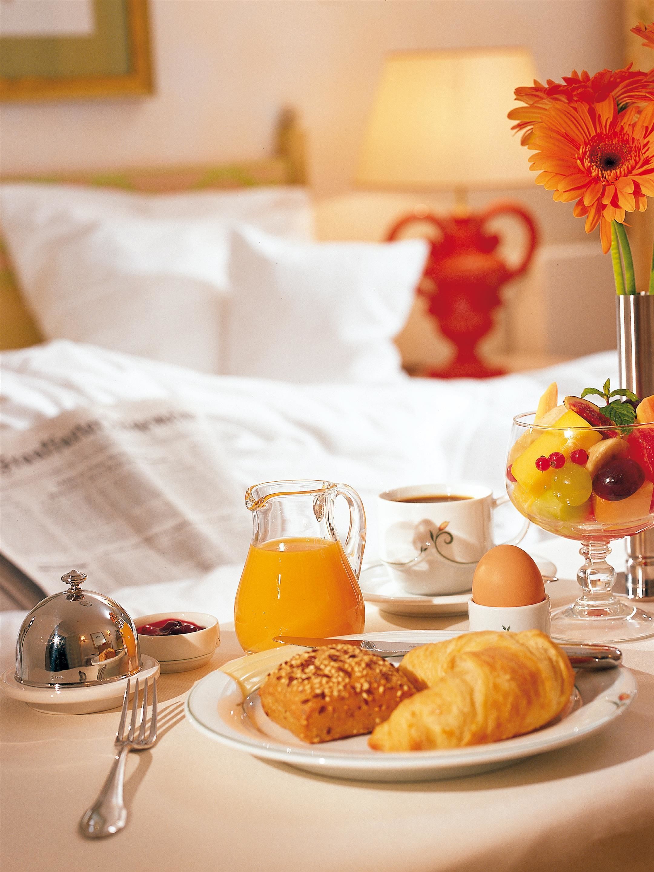 Une table dressée pour le petit-déjeuner avec des croissants, un saladier de fruits, une tasse de café et une carafe de jus d’orange.