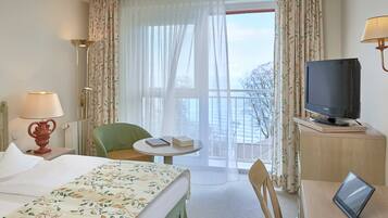 Ein Hotelzimmer mit Bett, Schreibtisch mit Laptop, Fernseher, Stuhl, Tisch und Vorhängen.