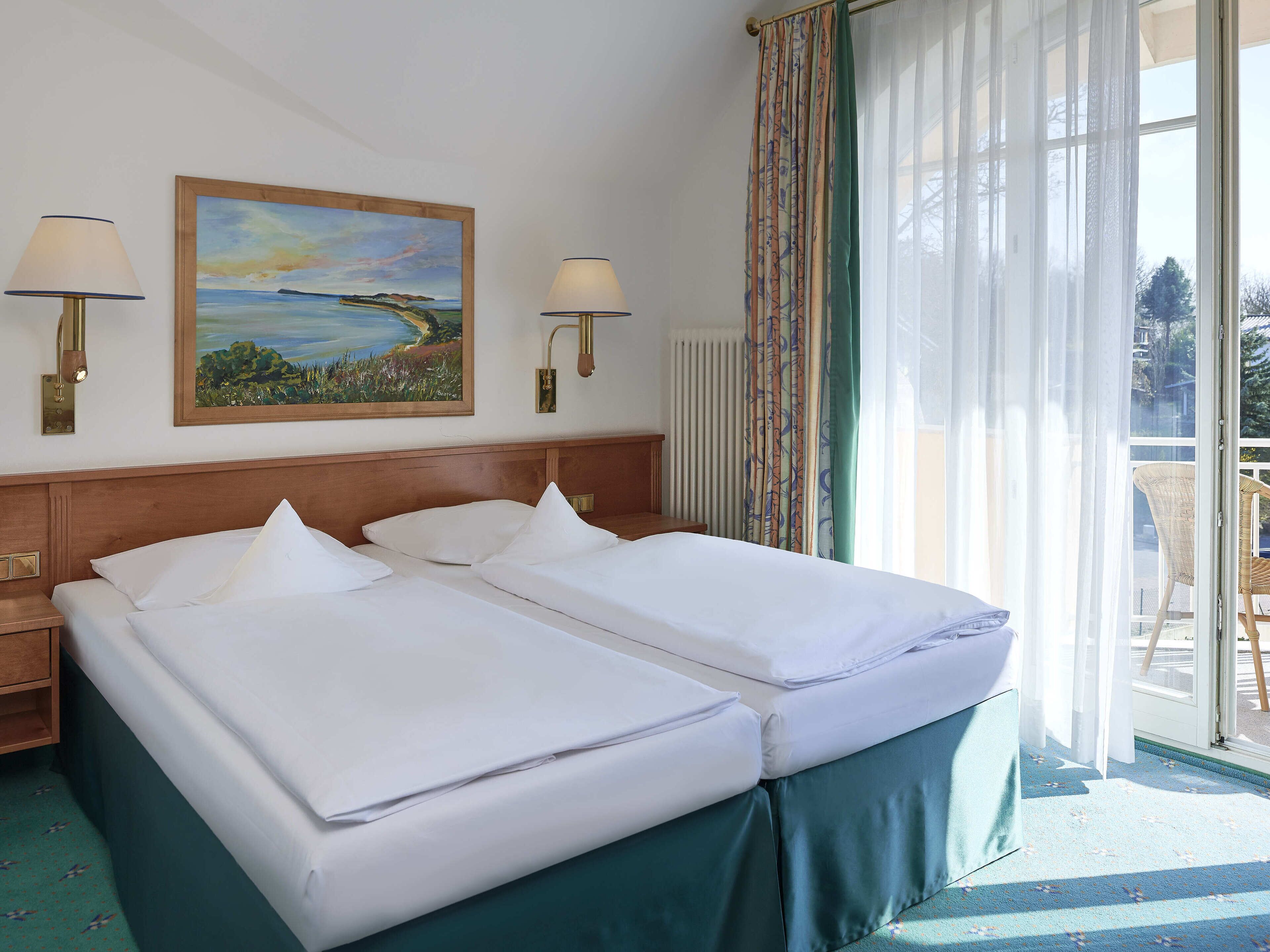 Une chambre d’hôtel avec deux lits, un tableau au mur et une vue sur l’extérieur par la fenêtre.