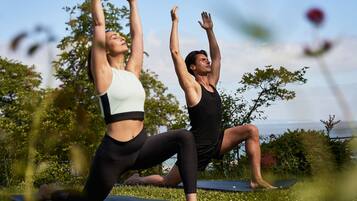 Två personer utövar yoga på yogamattor utomhus.
