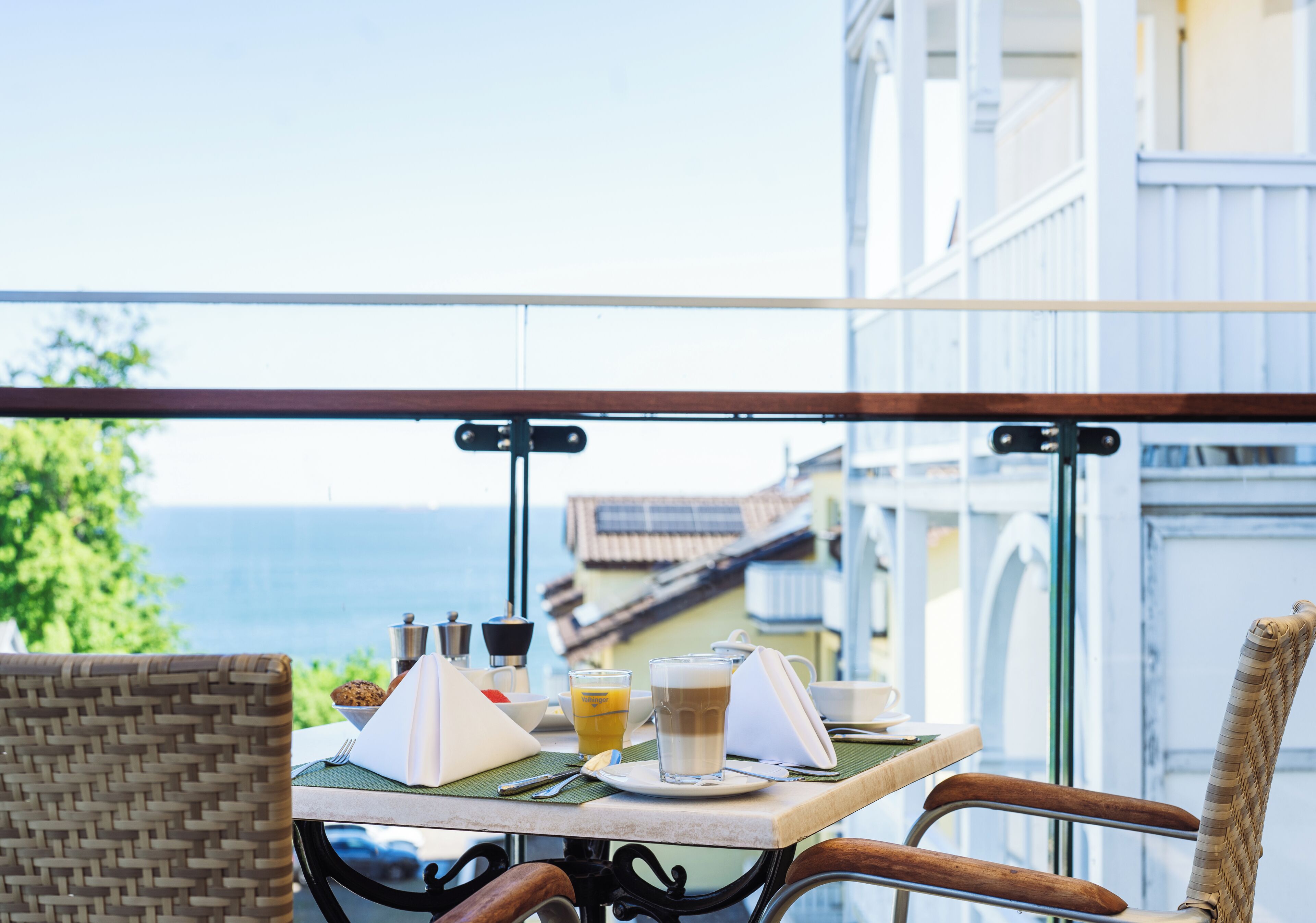 A balcony table with breakfast items, a view of the sea, and a wicker chair.