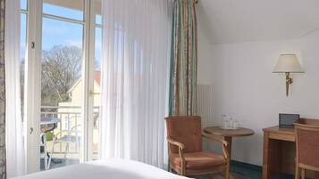 Ein Hotelzimmer mit Bett, Sessel, Nachttisch, Lampe und Blick nach draußen.