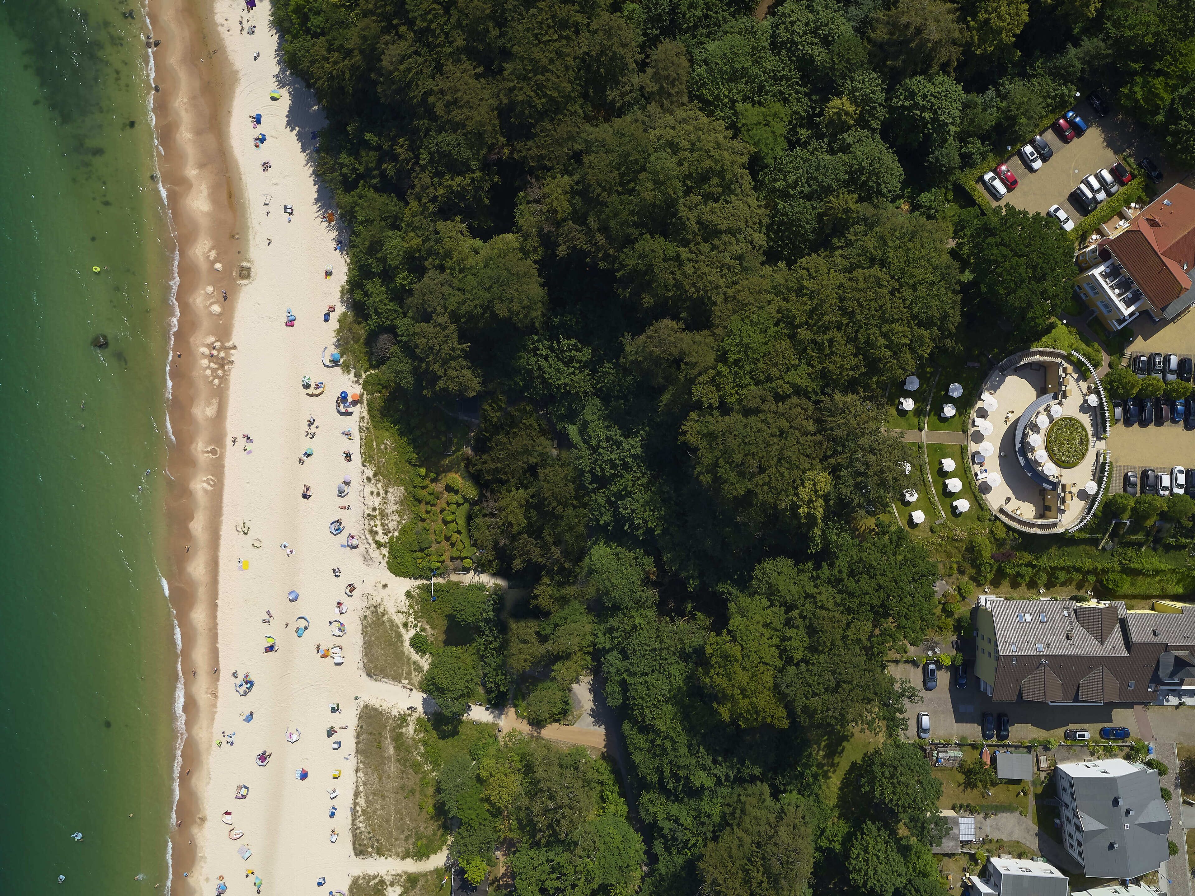 An aerial view of a beach with a parking area and a building with a circular courtyard.