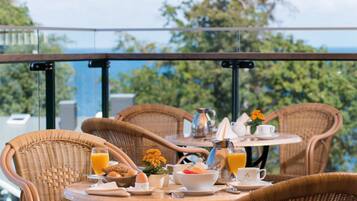 Desayuno en un balcón con sillas de mimbre, una mesa y vistas a la vegetación y un cuerpo de agua.
