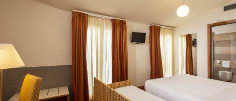 Habitación de hotel con cama, escritorio, silla, televisor y baño.