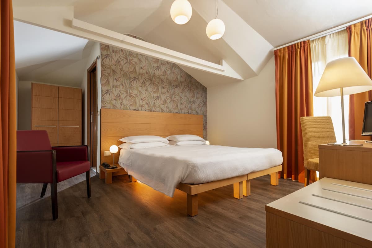 A hotel room with a bed, a desk, a chair, a nightstand, and a lamp.