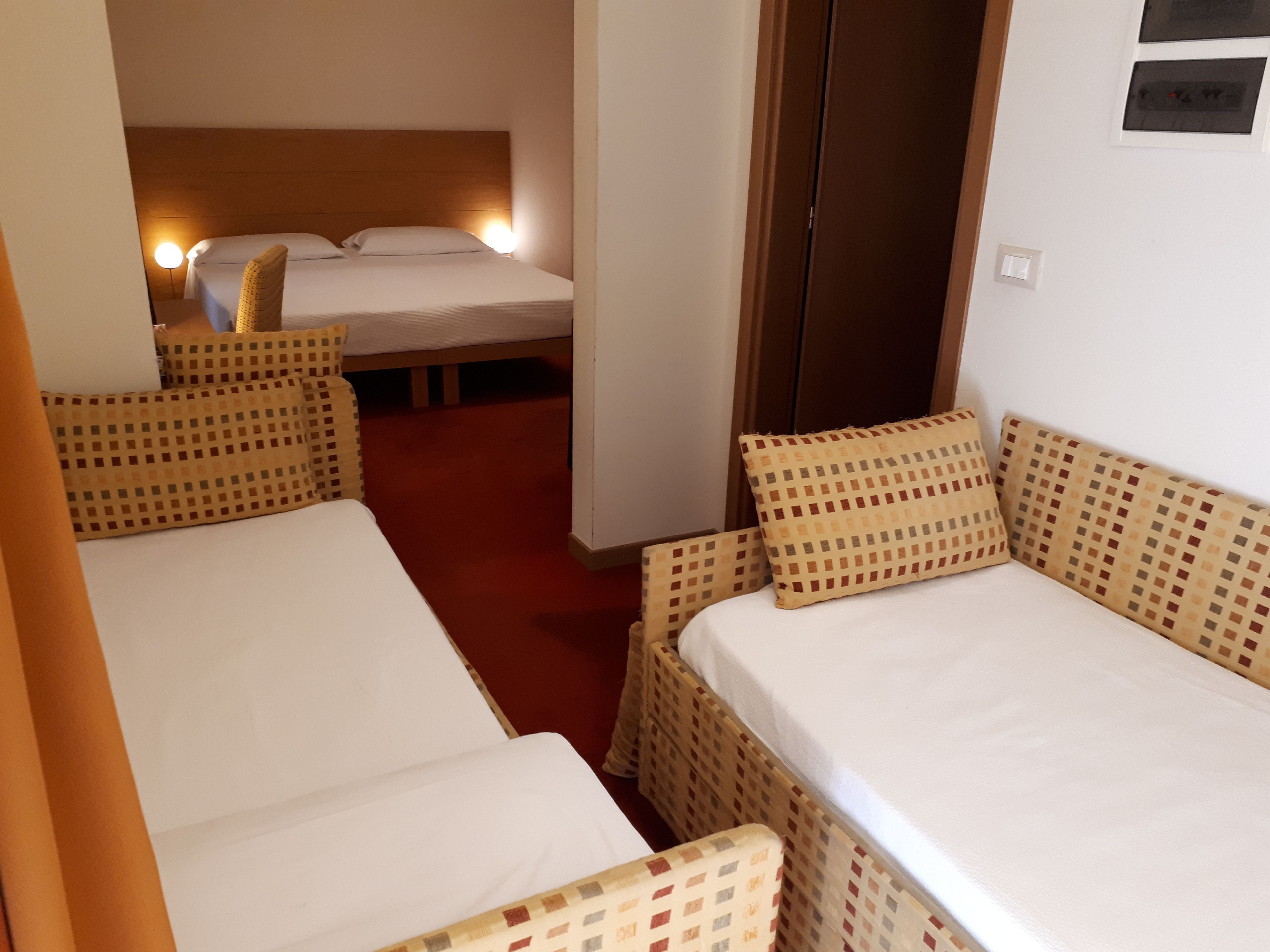 A hotel room with two single beds, a wooden headboard, a red carpet, and a small table.