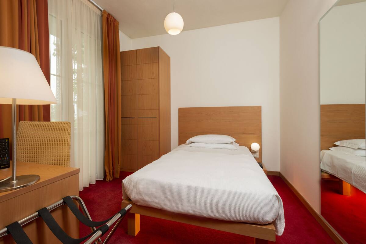 A hotel room with a wooden bed, a desk with a lamp, a chair, and a large mirror.