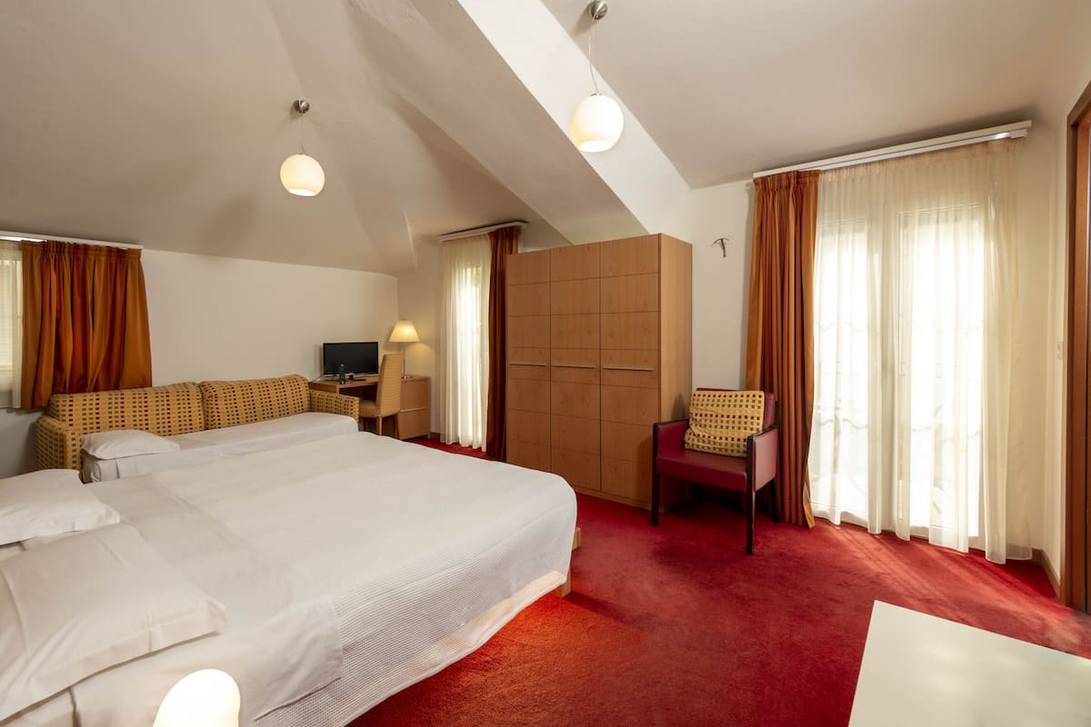 A hotel room with a large bed, a desk, a chair, and a wardrobe.