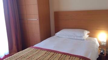 Una habitación de hotel con cama, cabecera de madera, mesita de noche con lámpara y armario.