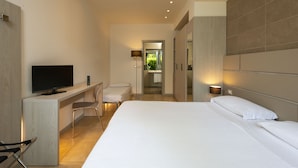 Una habitación de hotel moderna con una cama grande, un escritorio con televisor de pantalla plana, una silla y un baño privado.