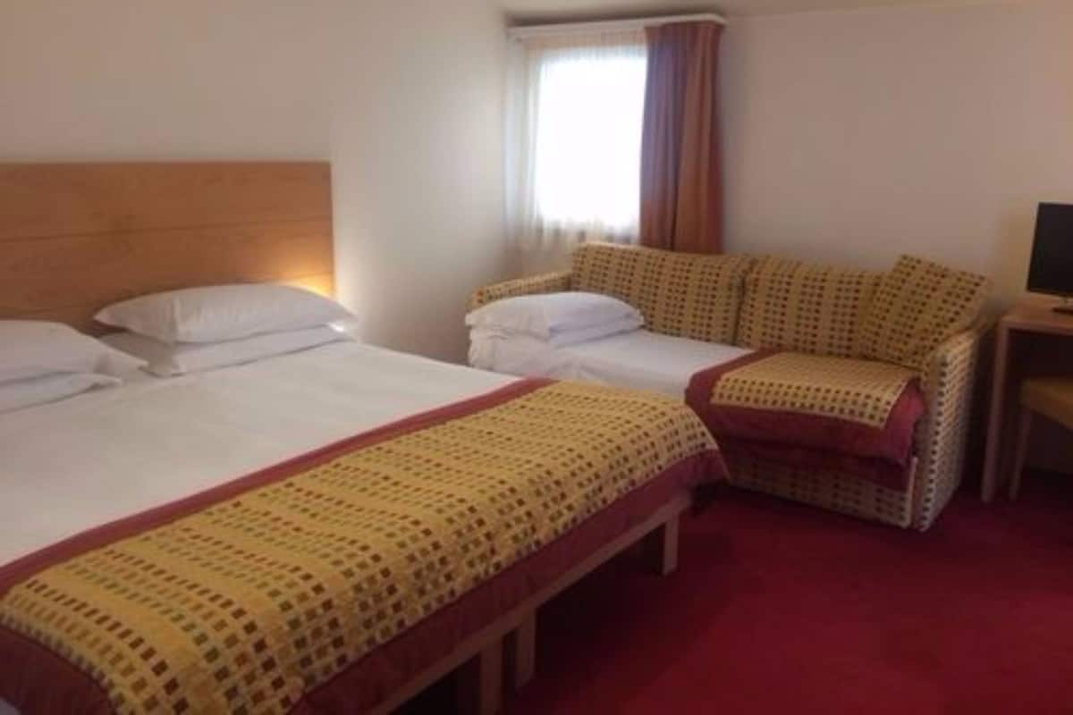 A hotel room with two beds, a sofa, a TV, and a window with curtains.