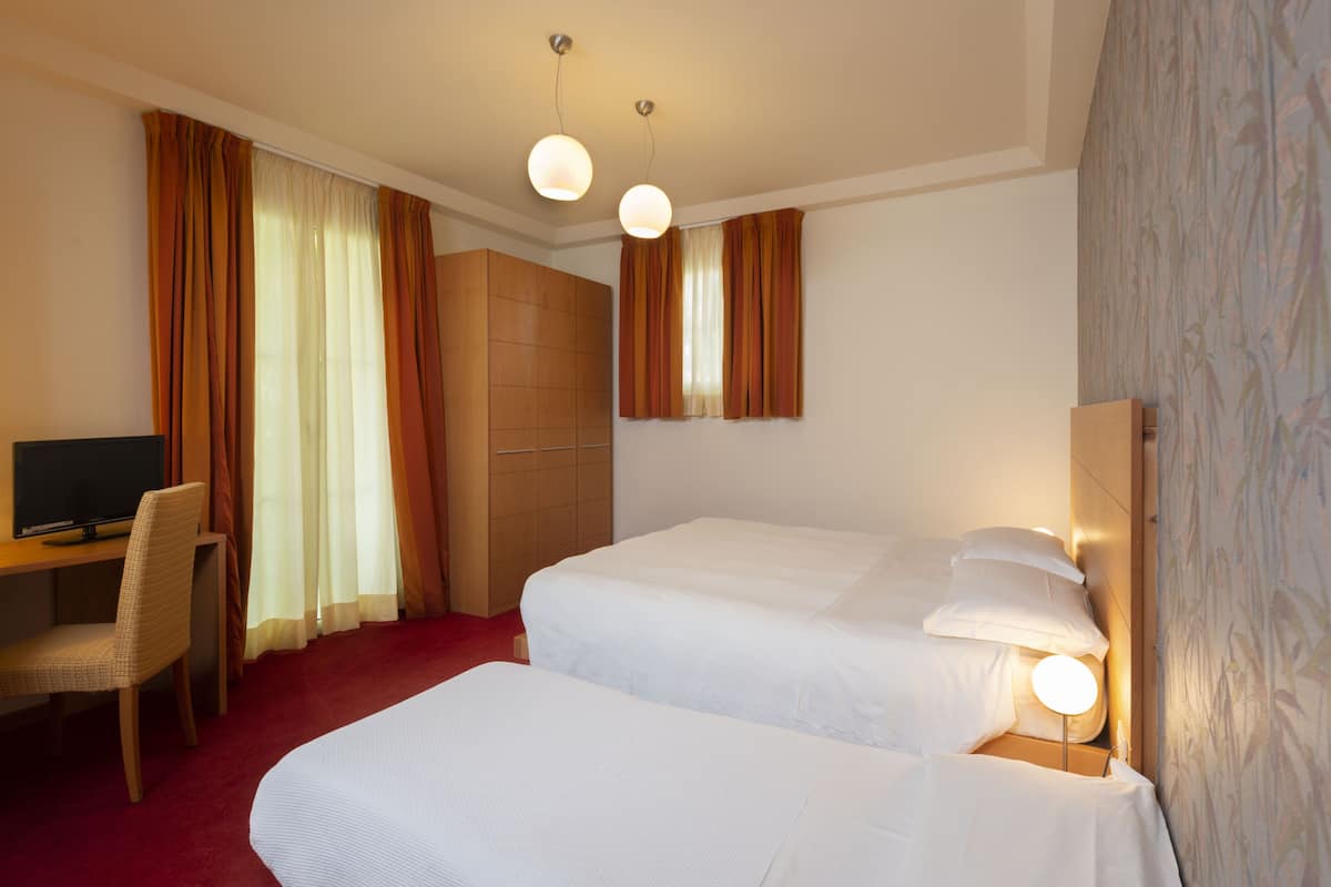 A hotel room with two beds, a desk, a chair, and a television.