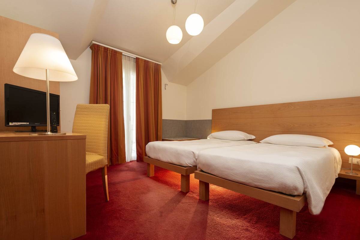 A hotel room with a wooden bed, a desk with a lamp, a television, and a chair.
