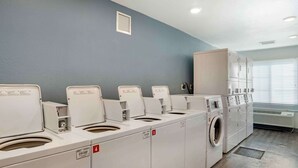 Un cuarto de lavandería con varias lavadoras y secadoras, un sistema de ventilación y una pared gris.