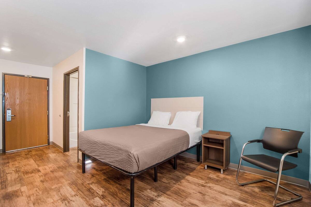 Een slaapkamer met een bed, een nachtkastje, een stoel en een houten deur.