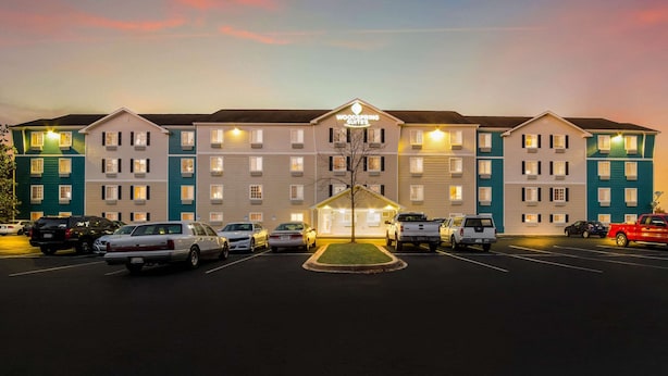 Een meerlaags hotel met een centrale ingang, parkeerplaats en heldere lucht.