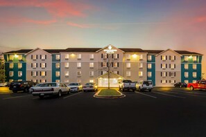A multi-story hotel with a central entrance, parking lot, and a clear sky. - WoodSpring Suites North Charleston Airport I-526 (North Charleston)
