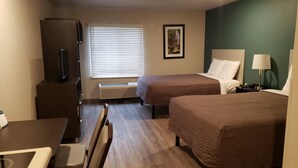 A hotel room with two beds, a desk, a chair, a TV, and a window with blinds. - WoodSpring Suites Kansas City Lenexa (Lenexa)