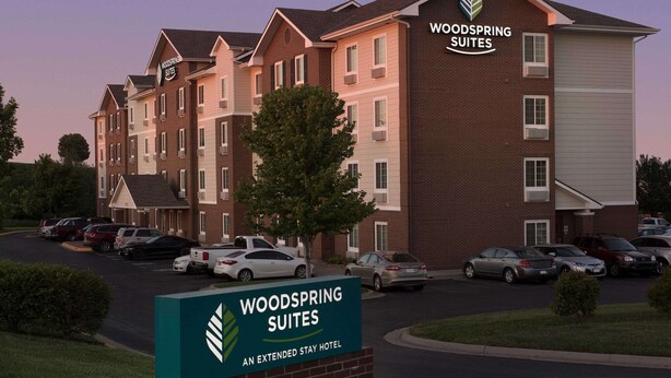 A multi-story hotel with a sign reading "Woodspring Suites" and "An Extended Stay Hotel." - WoodSpring Suites Kansas City Lenexa (Lenexa)