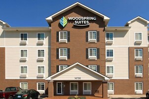 Un hotel de varios pisos con un llamativo letrero que dice "Woodspring Suites". Cuenta con fachada de ladrillo, múltiples ventanas y un techo plano.