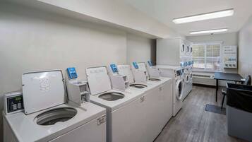 A laundry facility with multiple washing machines and dryers, a control panel, and a sign listing available detergents.