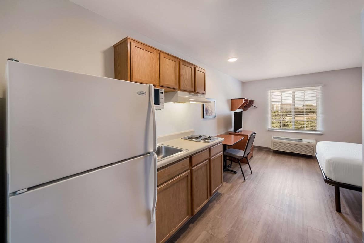 A compact kitchen with wooden cabinets, a white refrigerator, a stove, and a window with blinds.