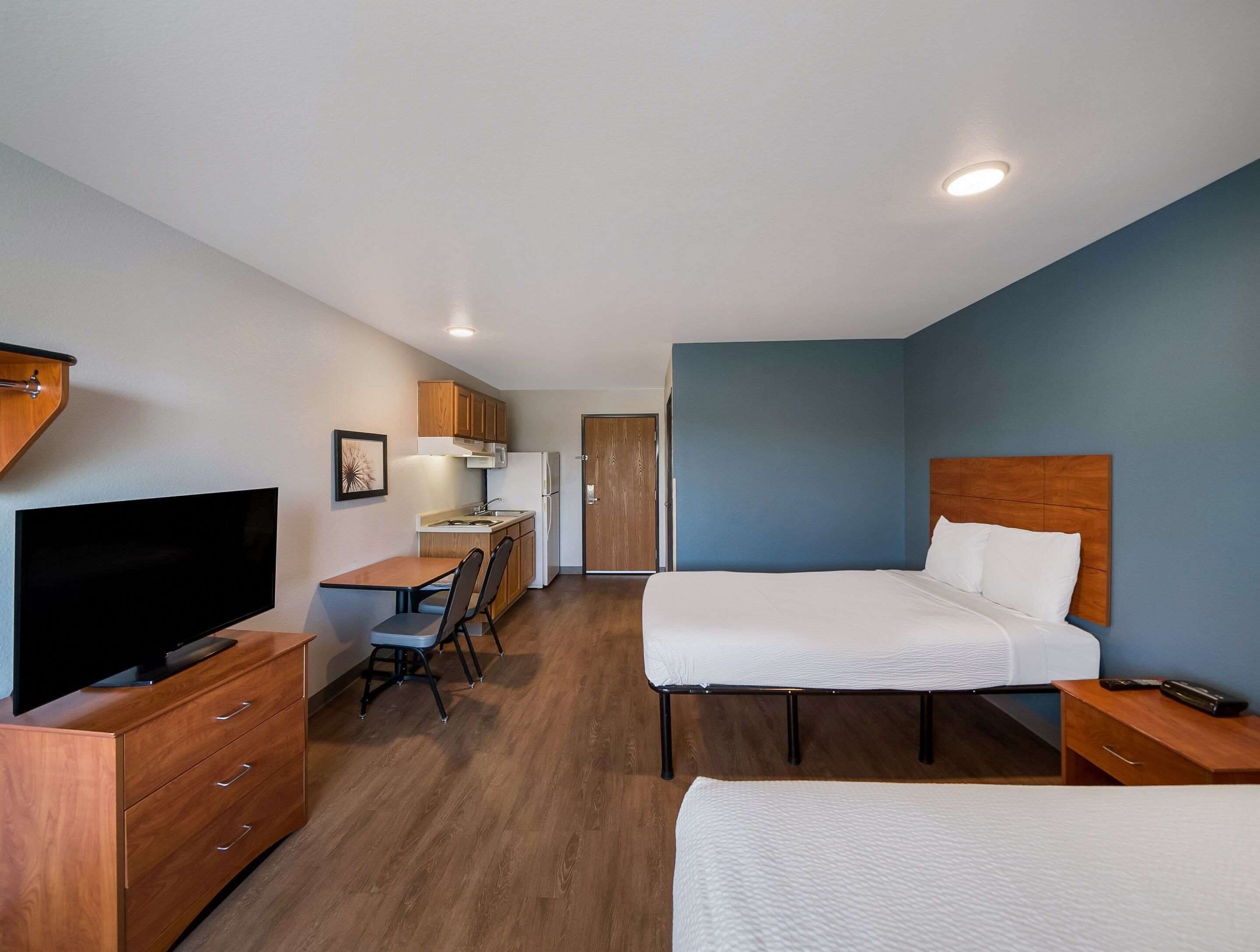 Habitación de hotel pequeña con cama, escritorio, silla, televisión y kitchenette.
