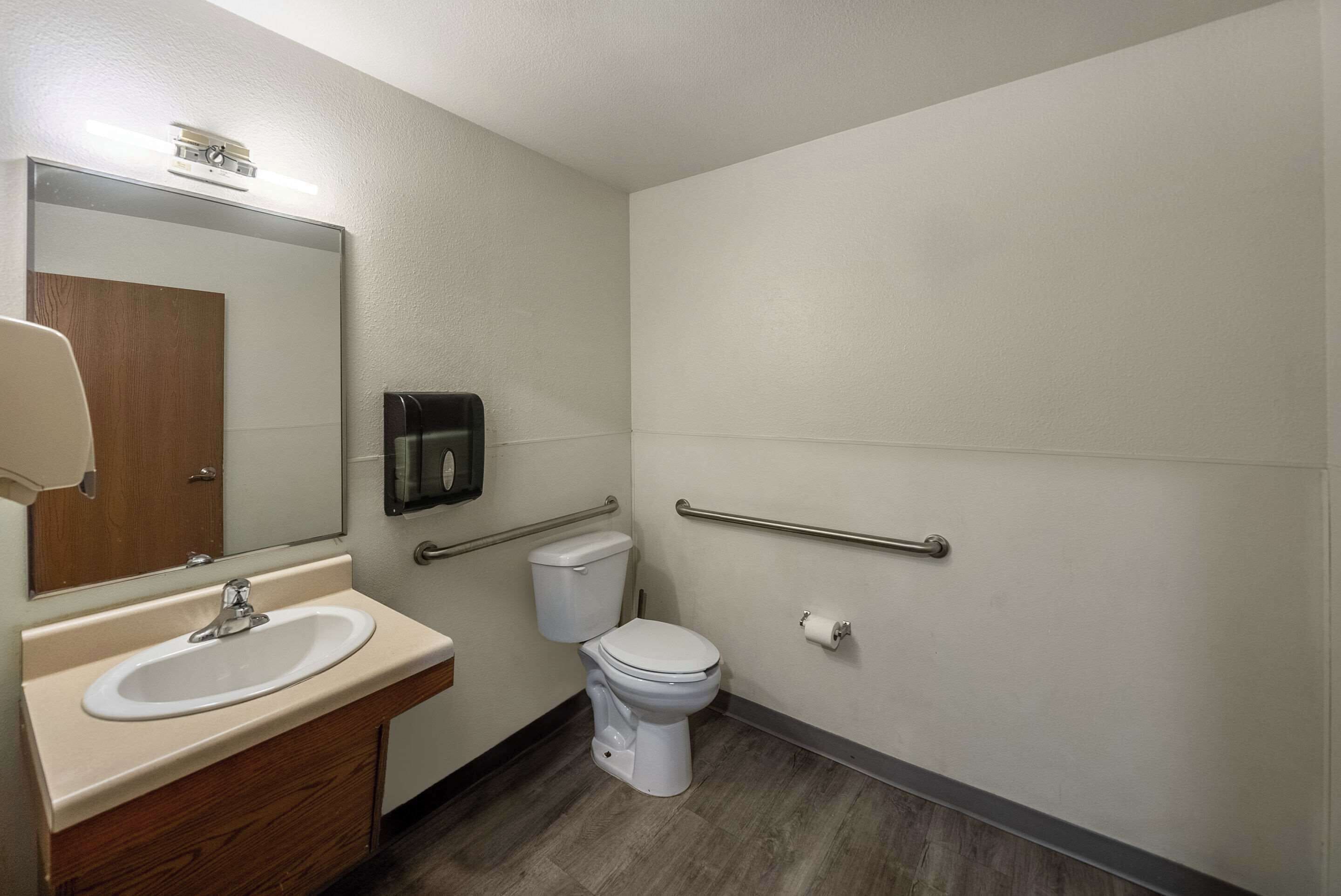 Ein Badezimmer mit Waschbecken, Spiegel, Toilette und Haltegriffen.